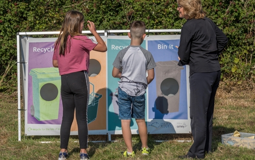 A woman and a boy and a girl stand opposite a poster showcasing different recycling containers.